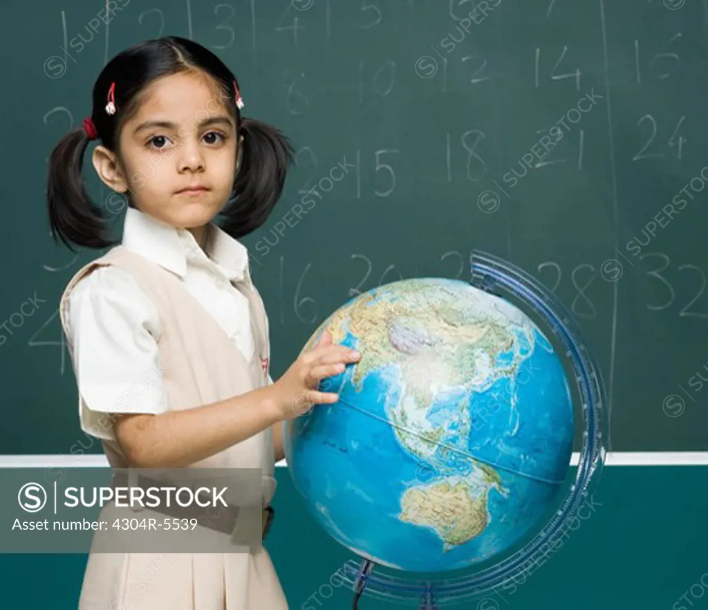 Girl (6-7) in classroom, holding globe, portrait