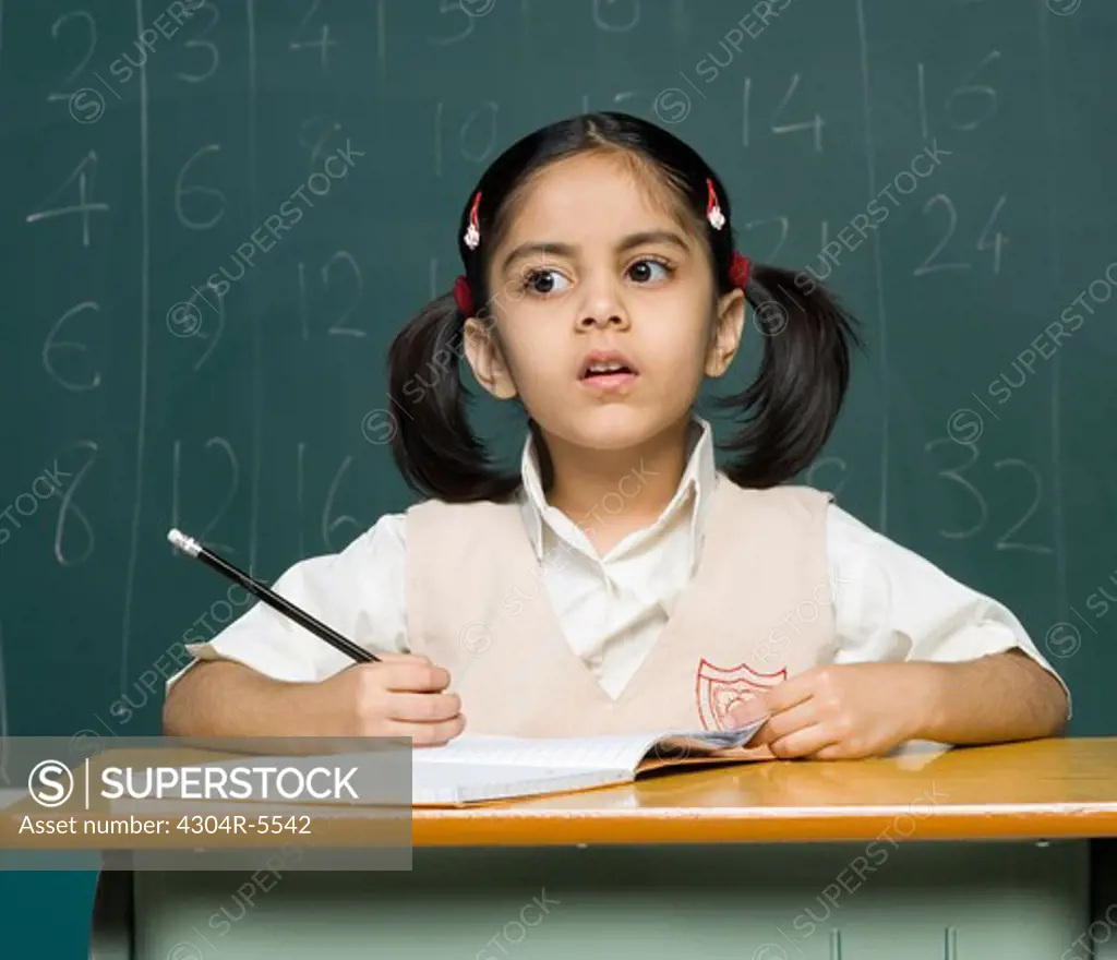 Girl (6-7) holding pencil, contemplating