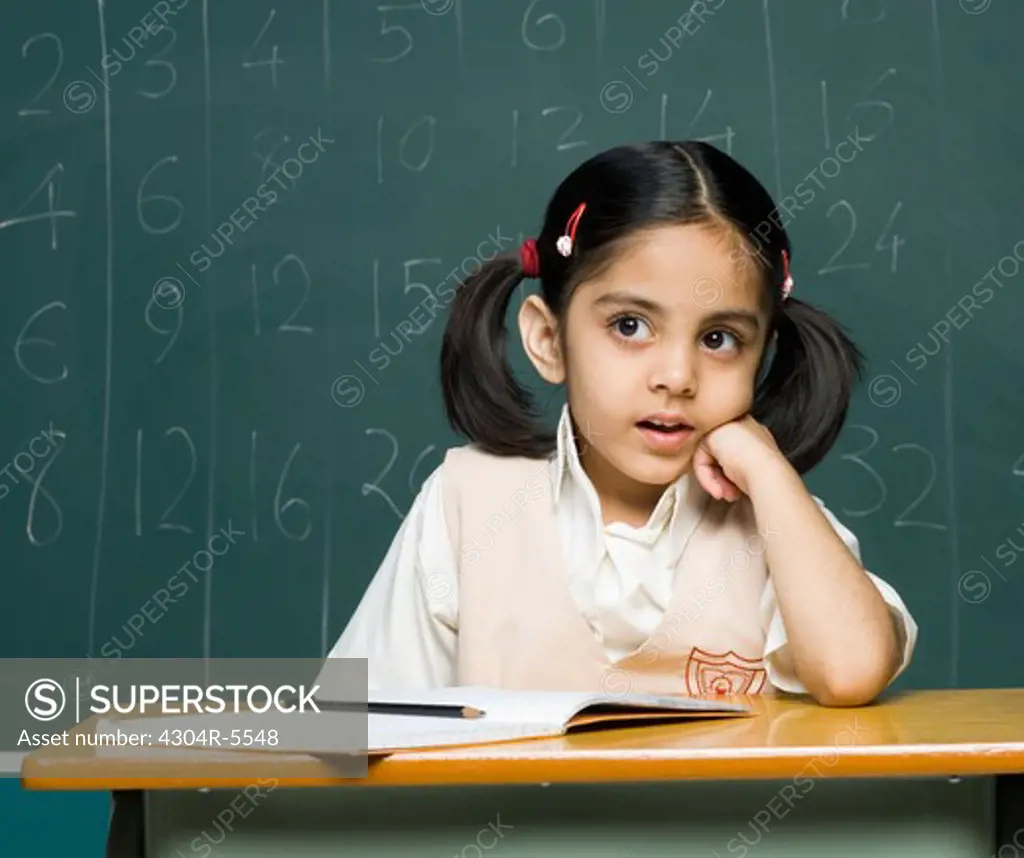Girl (6-7) sitting on desk, contemplating
