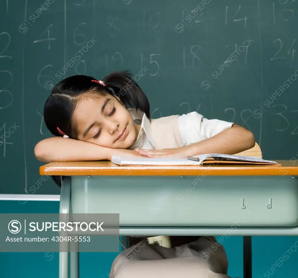 Girl (6-7) sleeping on desk in classroom