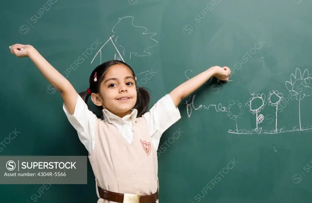 Girl (6-7) standing by board, arms raised, portrait