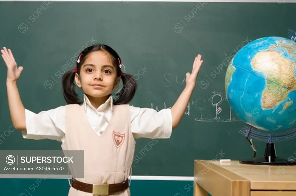 Girl (6-7) standing by board, arms raised, portrait