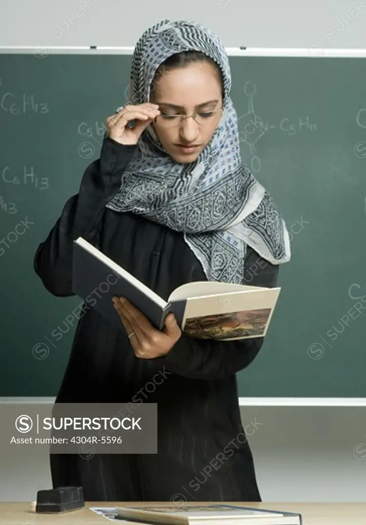 Teacher holding book against board at school