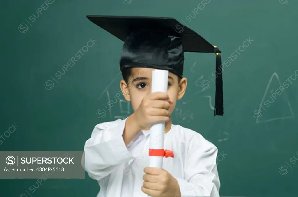 Boy (4-5) wearing mortarboard and holding degree, portrait