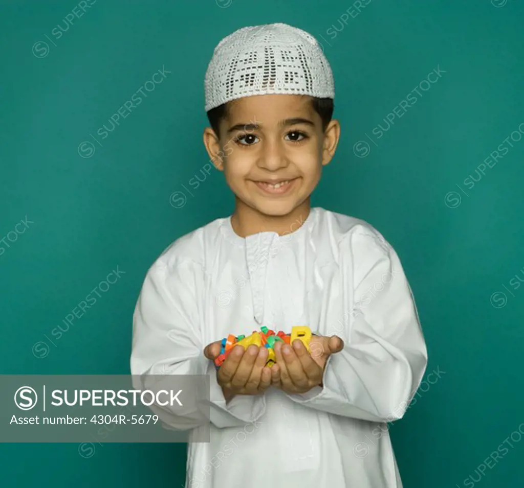 Boy (8-9) holding colorful alphabets, smiling, portrait
