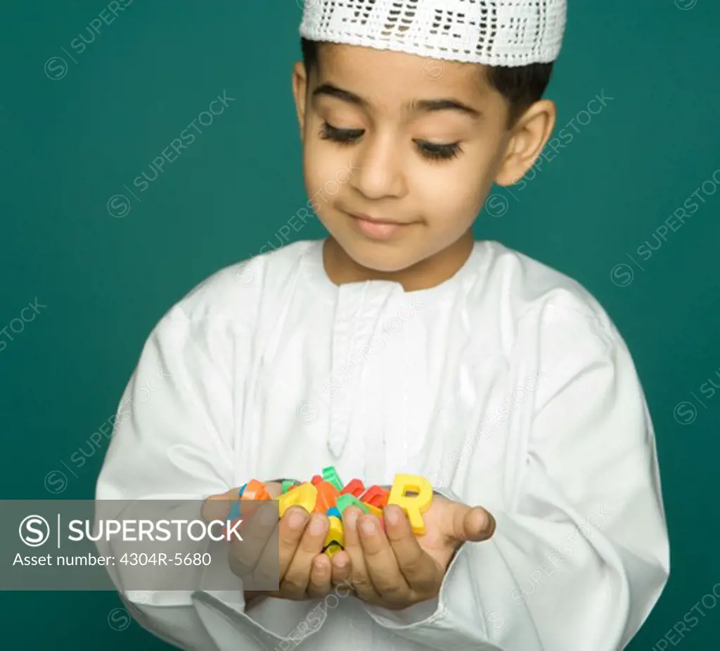 Boy (8-9) holding colorful alphabets, smiling, portrait