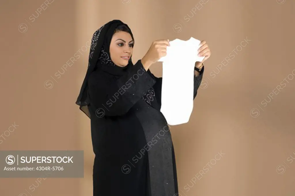 Pregnant woman holding baby cloth, smiling