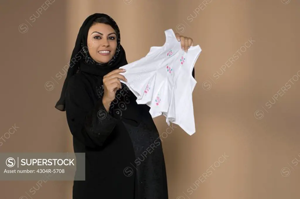 Pregnant woman holding baby cloth, smiling, portrait