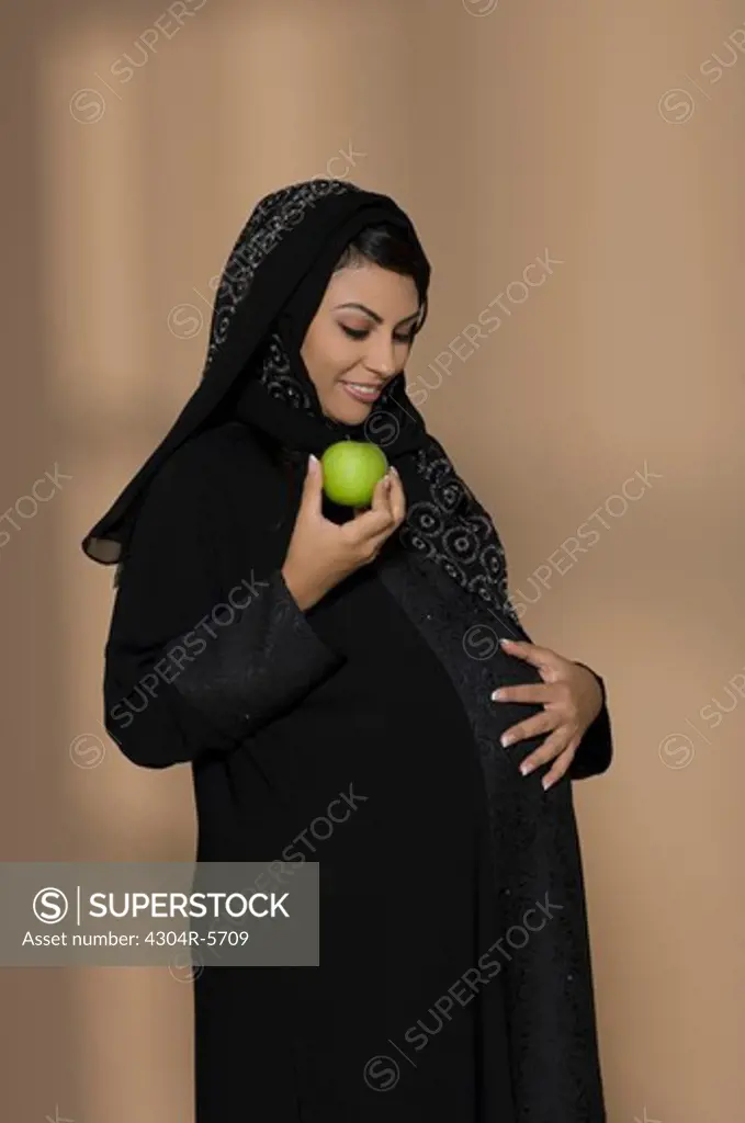 Pregnant woman holding green apple and touching abdomen