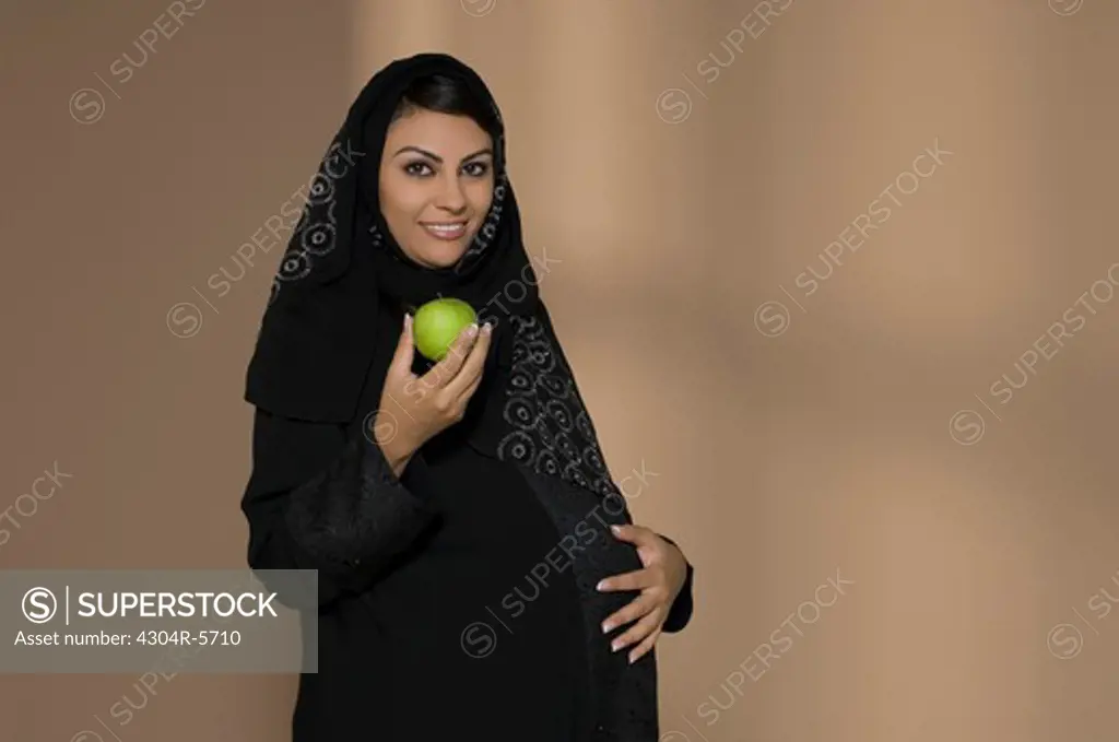 Pregnant woman holding green apple and touching abdomen, portrait