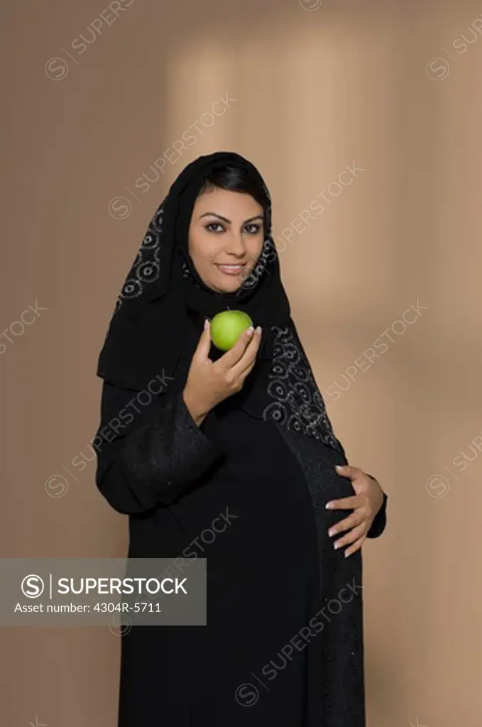 Pregnant woman holding green apple and touching abdomen, portrait