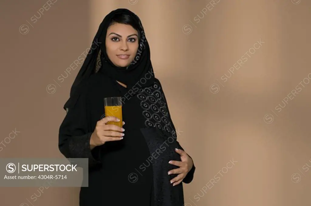 Pregnant woman holding glass of juice and touching abdomen, portrait
