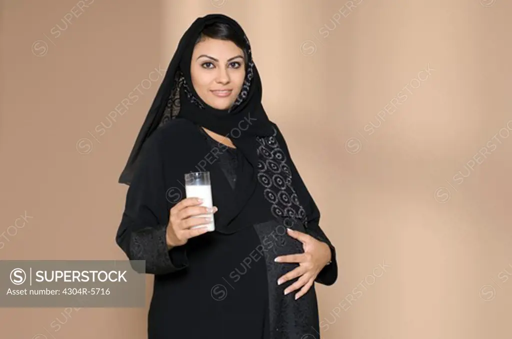 Pregnant woman holding glass of milk and touching abdomen, portrait