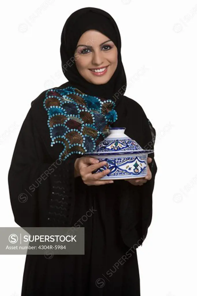 Young woman holding lidded bowl, smiling, portrait