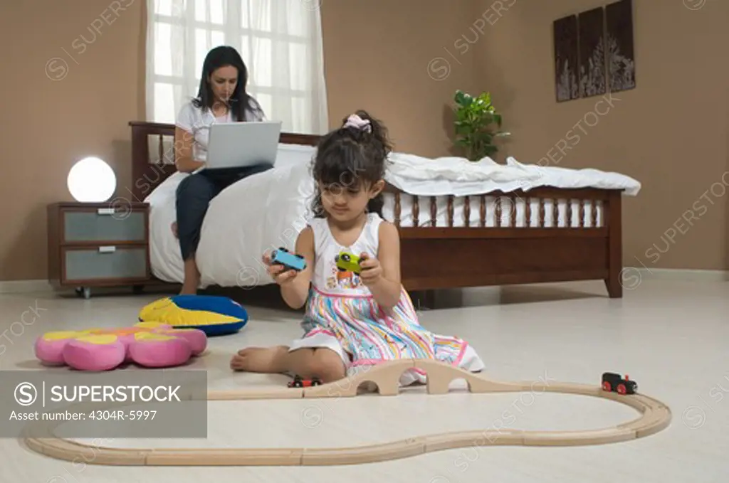 Daughter (3-4) playing with toys while mother using laptop