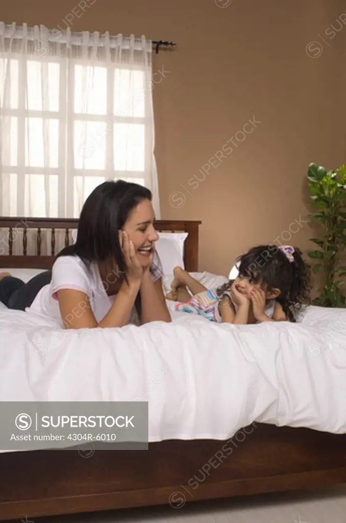 Daughter (3-4) with mother lying on bed