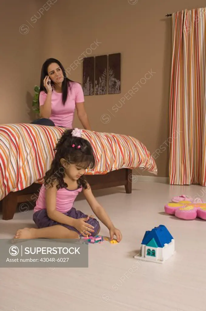 Daughter (3-4) playing with toys while mother talking on mobile phone