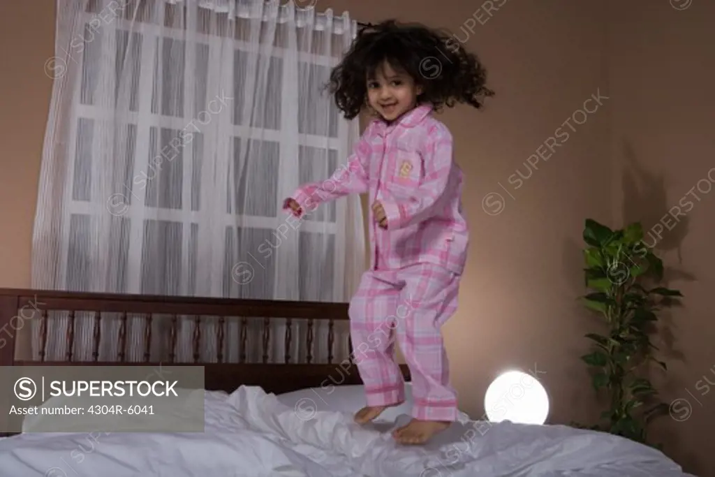 Girl (3-4) jumping on bed