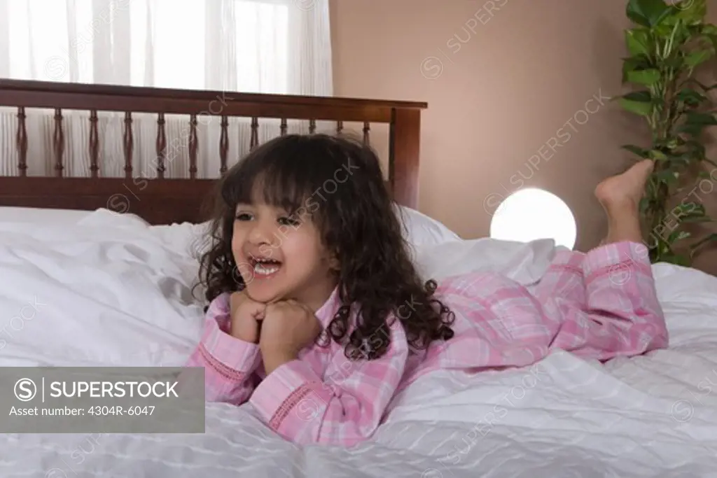 Girl (3-4) lying on bed, smiling