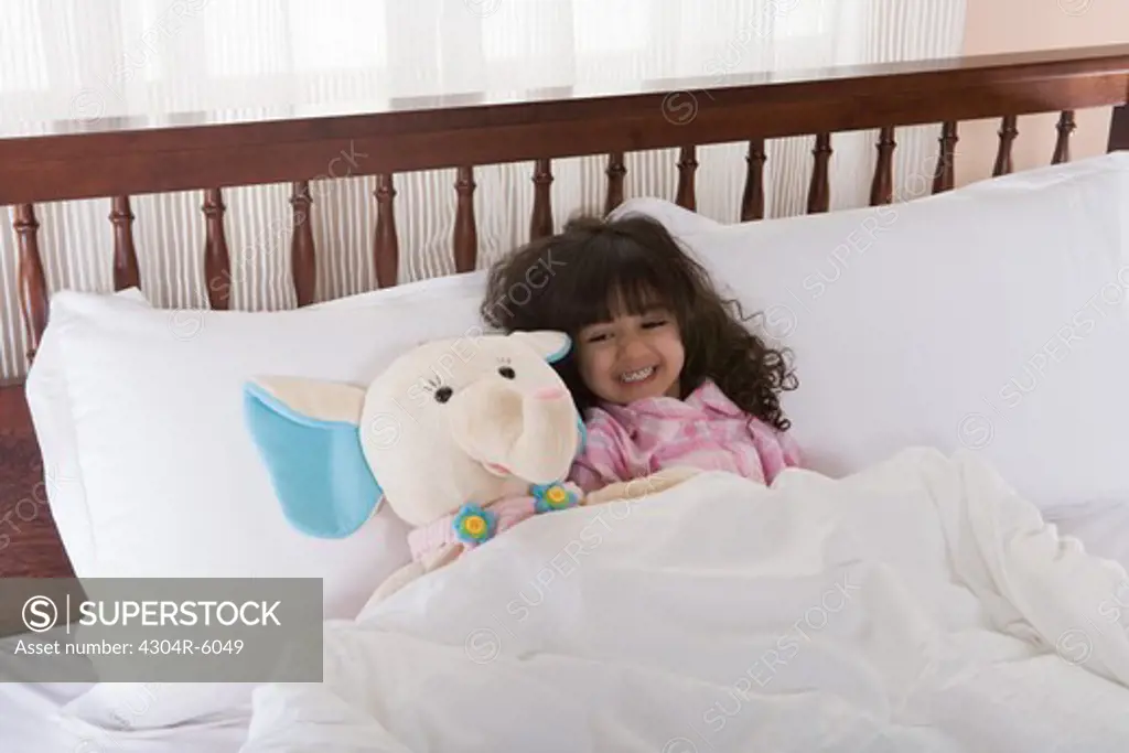 Girl (3-4) lying on bed by toy, smiling