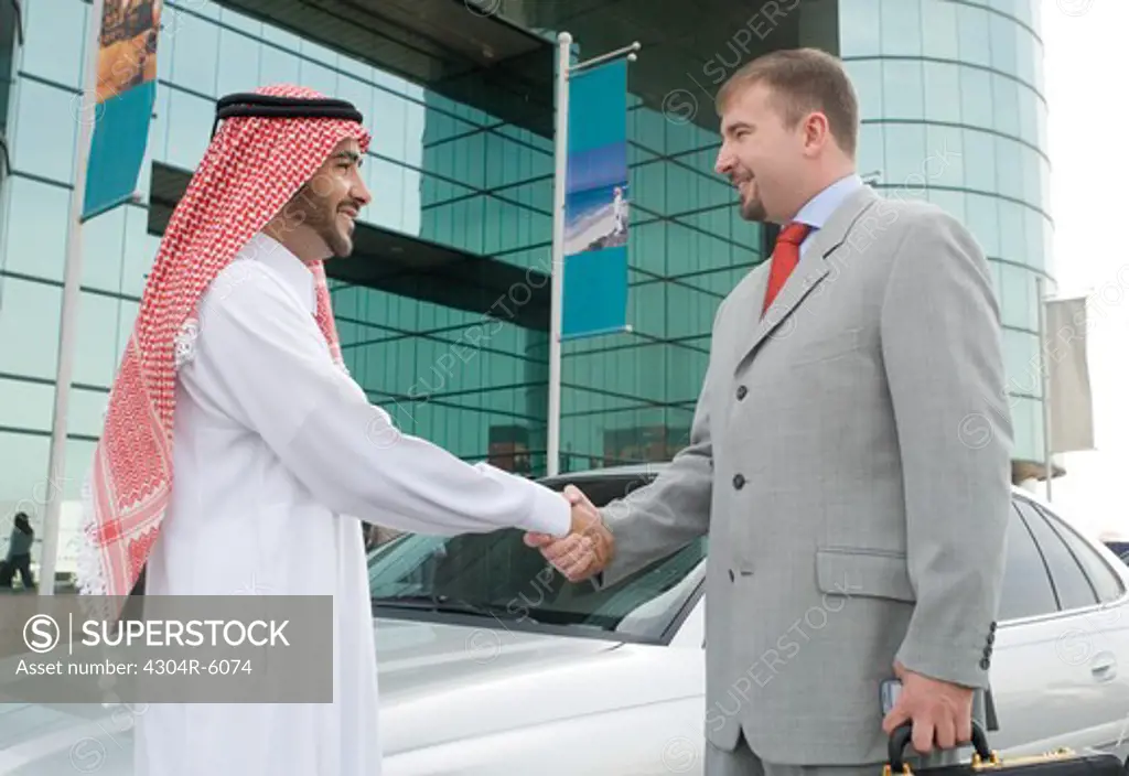 Businessmen shaking hands by car, smiling