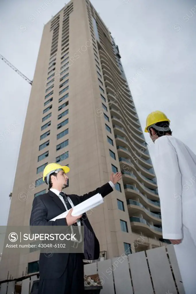 Businessmen holding blueprint gesturing at construction site, low angle view
