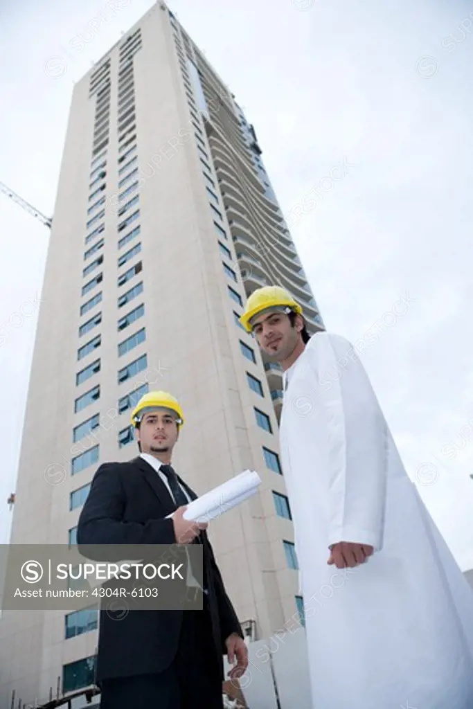 Businessmen standing with blueprints by building, low angle view, portrait