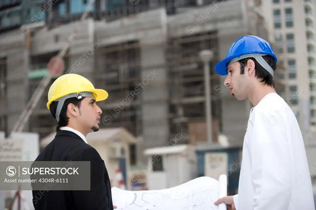Businessmen discussing blueprints at construction site, side view