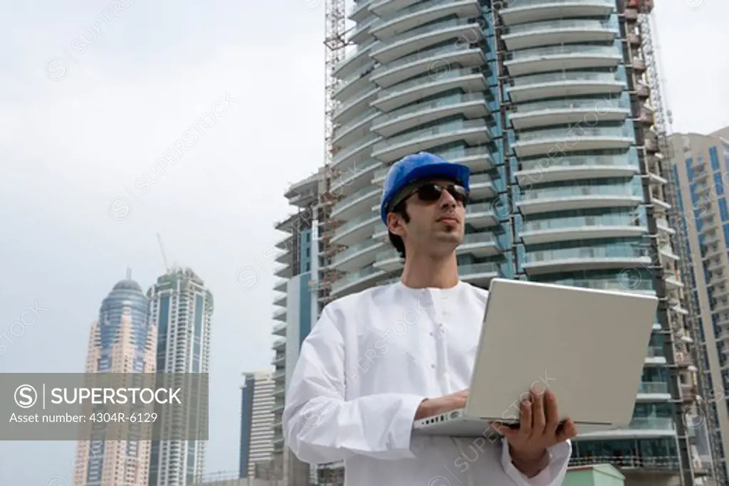 Businessman wearing hardhat and using laptop at construction site