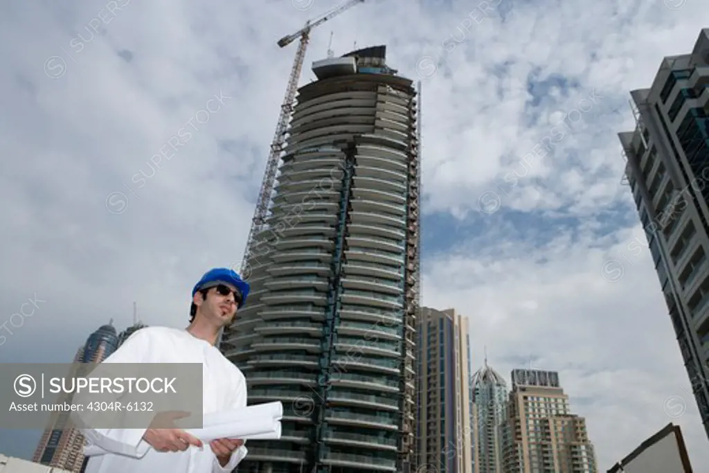 Businessman wearing hardhat and standing with blueprints at construction site