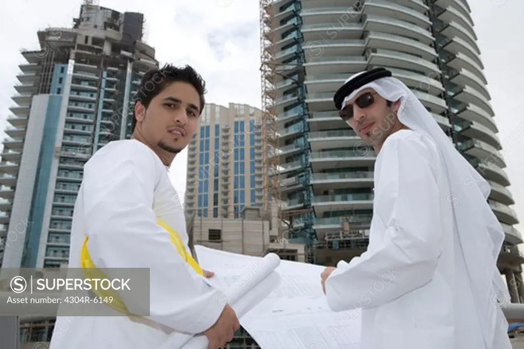 Businessmen with blueprints by railing with buildings in background, portrait