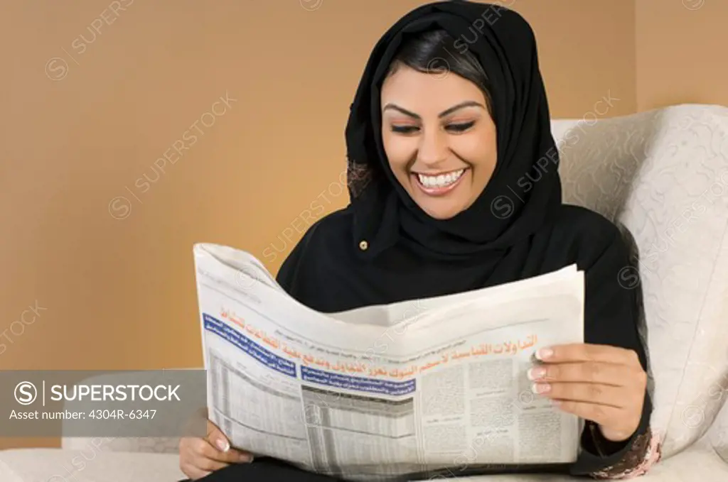 Young woman reading newspaper, smiling
