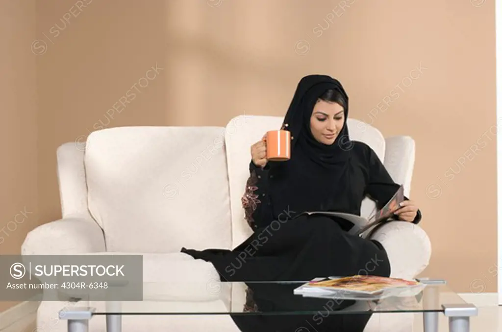 Young woman holding mug, reading magazine