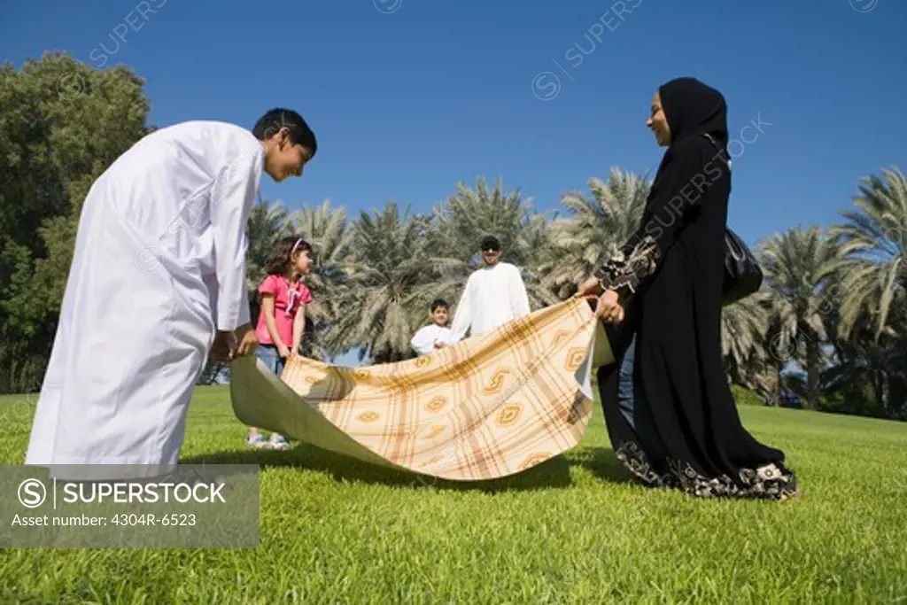 Mother with children spreading sheet on grass while father with son standing in background