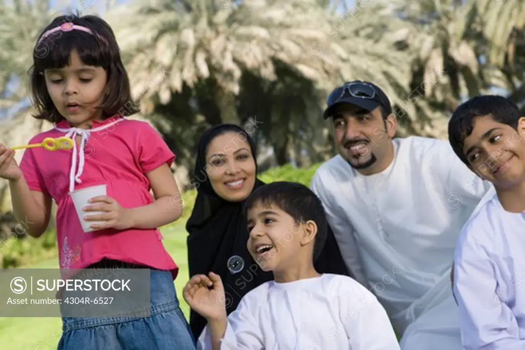Girl holding bubble wand while parents and children sitting together and smiling