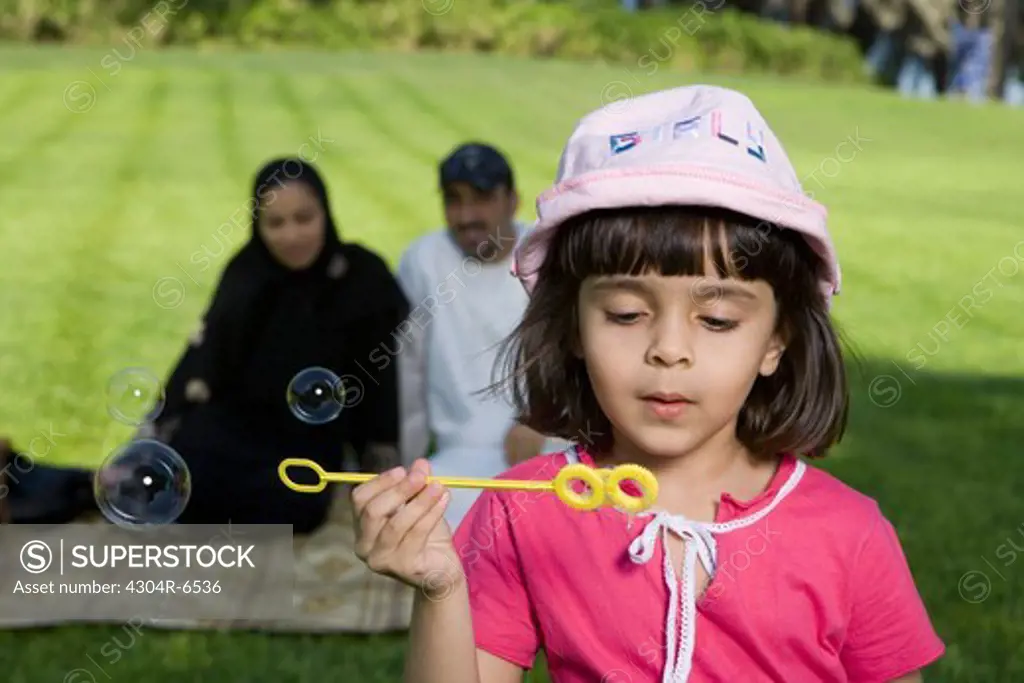 Girl holding bubble wand while parents sitting in background