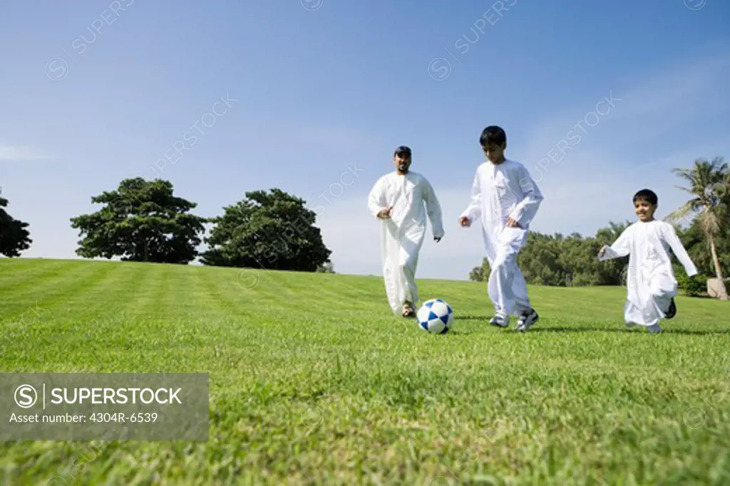 Father with sons playing football in park