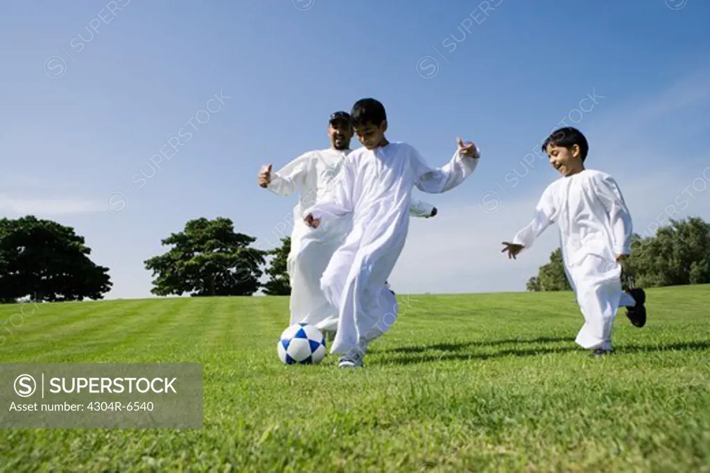 Father with sons playing football in park