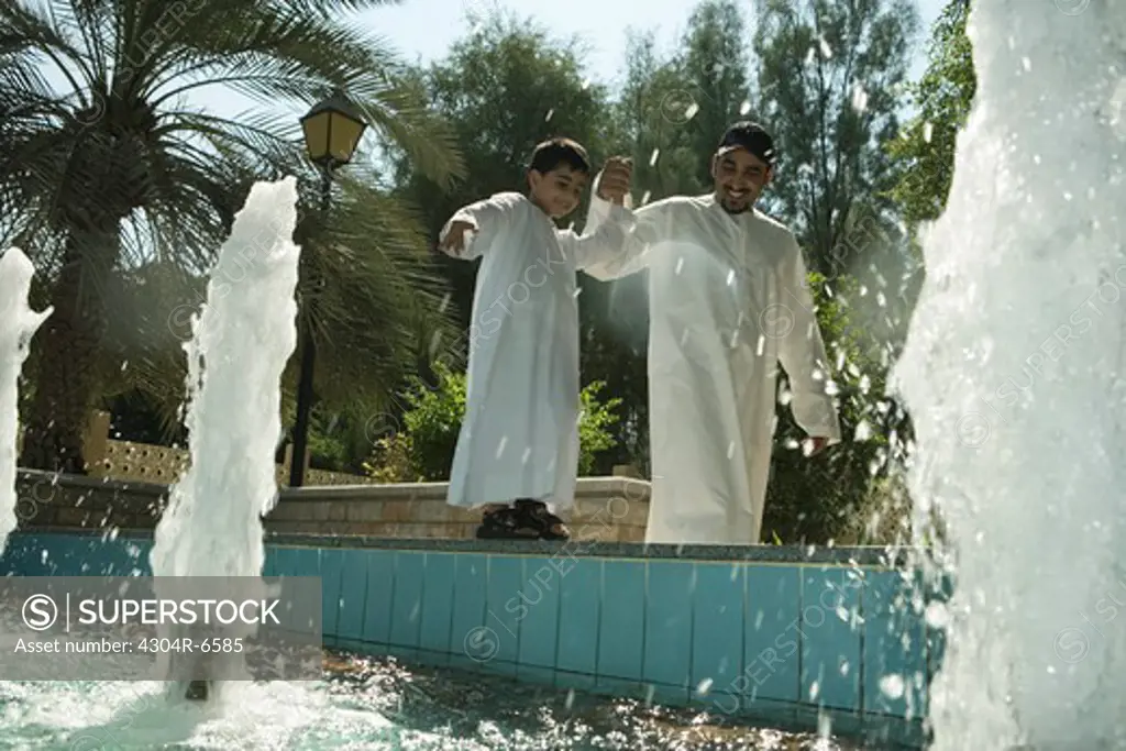 Father with son standing by fountain, smiling