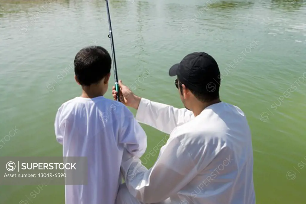 Father with son holding fishing rod, rear view