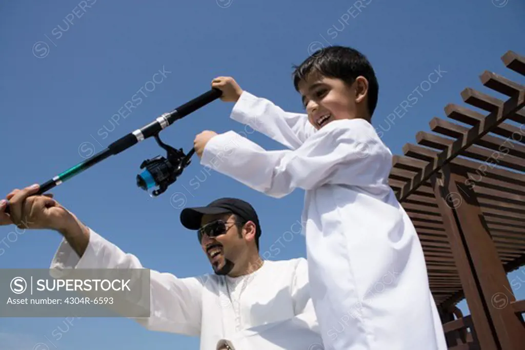 Father with son holding fishing rod, smiling, low angle view