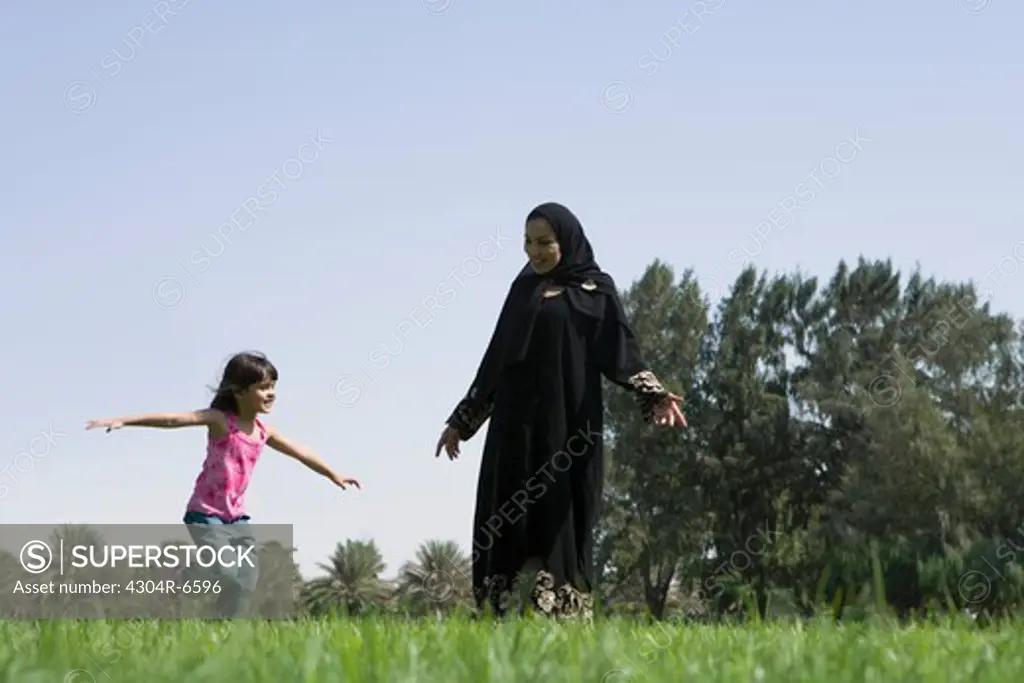 Mother and daughter with arms outstretched at park, smiling
