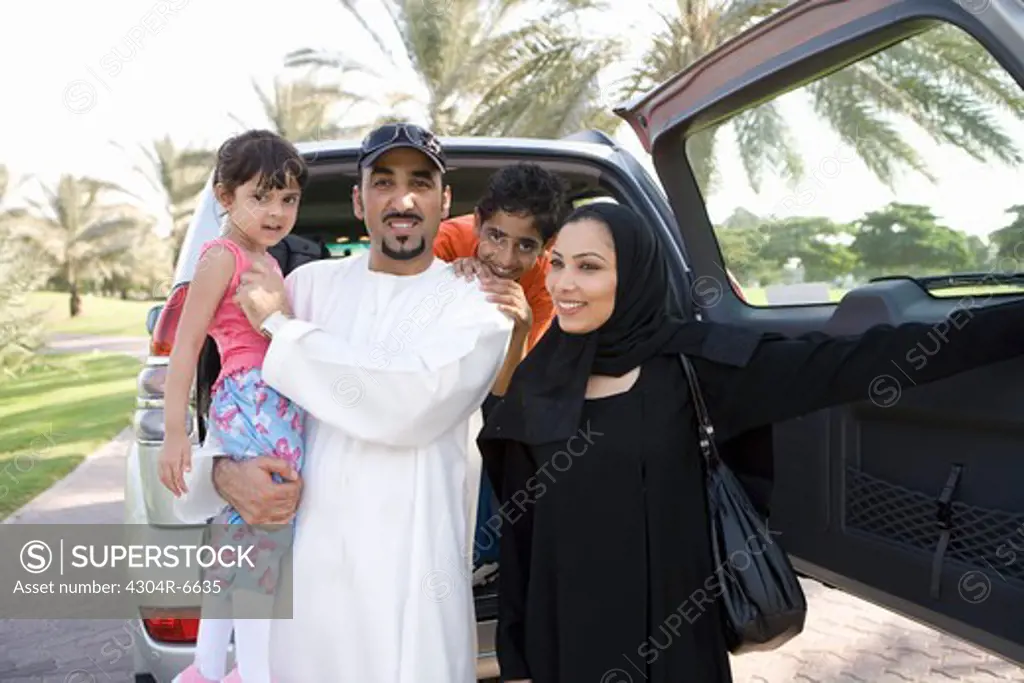 Father and mother with children standing in front of car, smiling