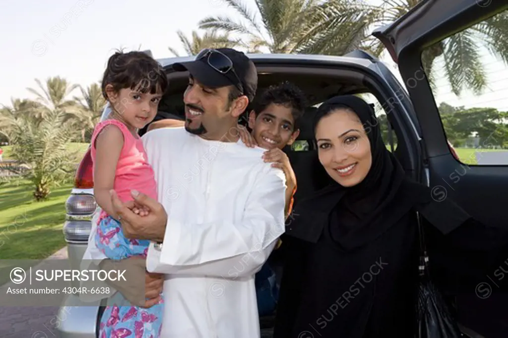Parents with children standing in front of car, smiling