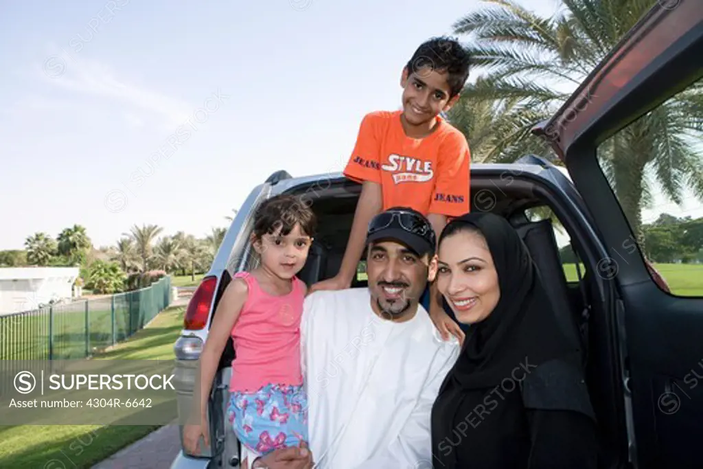 Parents and children standing in front of car, smiling, portrait