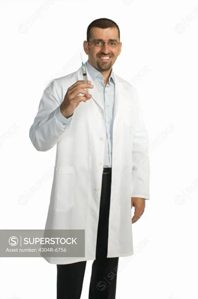 Doctor holding syringe standing against white background, smiling, portrait