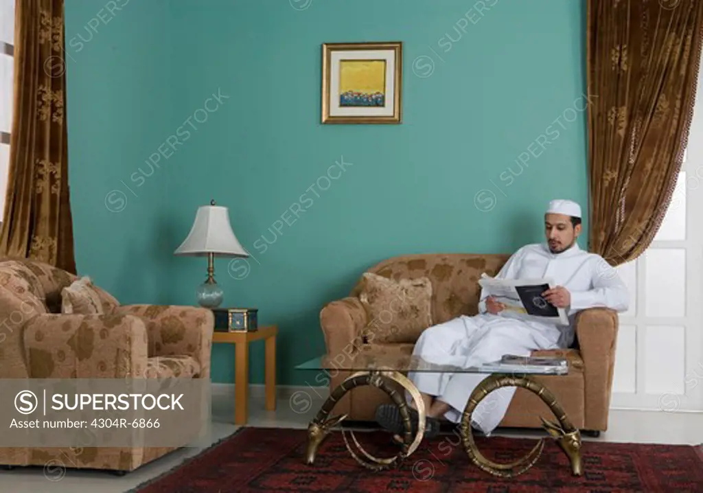 Arab man reading a newspaper in the living room