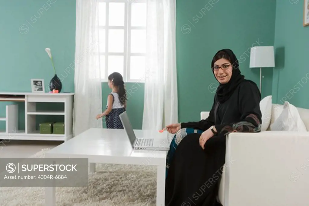 Arab mother working at home, daughter playing
