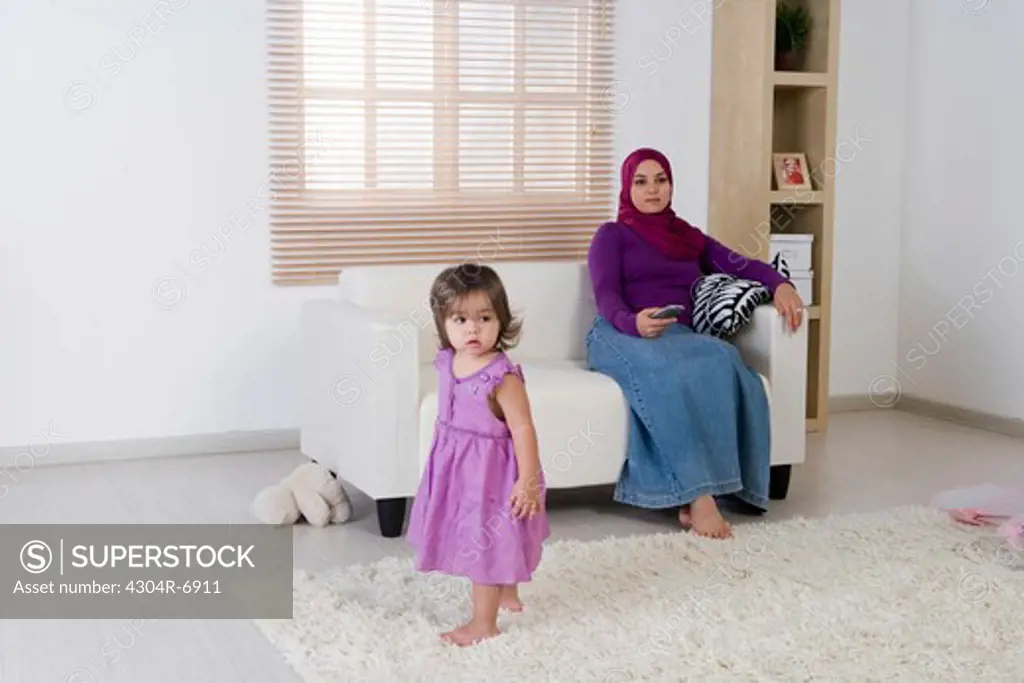 Mother holding the television remote control, daughter watching