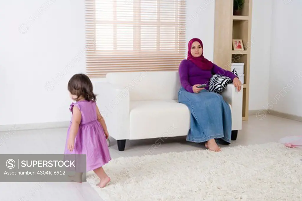Mother holding the television remote control, daughter walking around